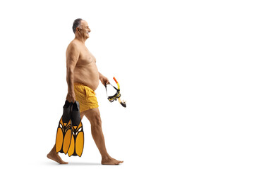Mature man in swimming shorts carrying mask and swimming fins and walking