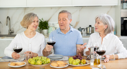 Happy pensioners gathered at the festive table - talking, discussing news and drinking red wine