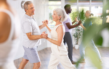 Dynamic mature attendees of dancing courses training poses of Waltz in dance hall