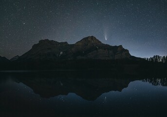 Night sky with stars over a mountain and its reflection in a calm lake, silhouette and a visible comet, Comet Neowise, Kananaskis Country, Alberta, Canada, North America