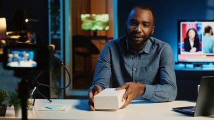 Fototapeta premium BIPOC tech content creator filming product unboxing of newly released smartphone, urging audience to purchase it too. Internet star payed by sponsor to show phone to subscribers