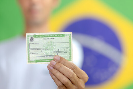 T&iacute;tulo de eleitor segurado por um eleitor brasileiro, documento essencial para participar das elei&ccedil;&otilde;es brasileiras. Brasileiro exercendo a sua cidadania ao votar. No fundo, a bandeira do Brasil.
