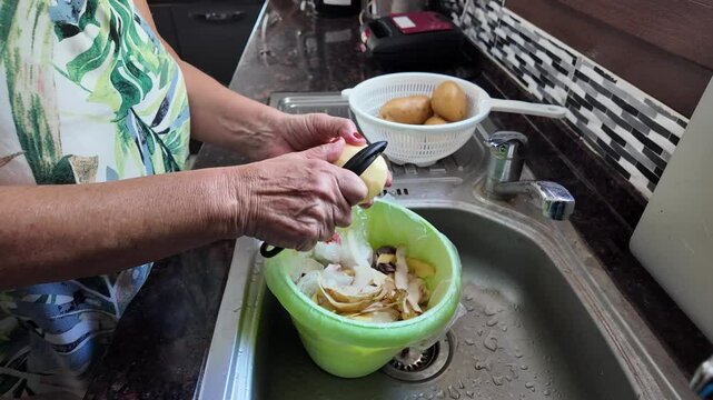 A woman's hands are peeling potatoes over the kitchen sink, peeling vegetables for cooking in the kitchen. Water flows from the tap. High quality 4k footage