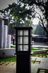 Close-up of a modern street lamp post with a sleek black frame, situated in a serene urban park with blurred trees and pathways in the background. Ideal for urban design and outdoor themes