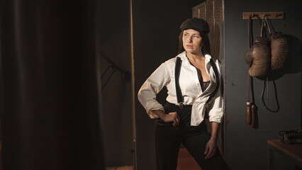 Caucasian woman in a Peaky Blinders style men's suit posing in a retro gym.