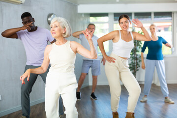 Dynamic young and mature attendees of dancing courses training Rock and Roll dance poses in...