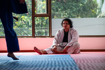 Latin long hair judo fighter resting in dojo with some trees at background