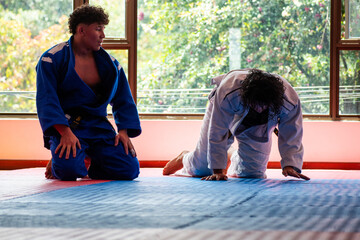Judo fighters resting after combat in dojo with big windows at background