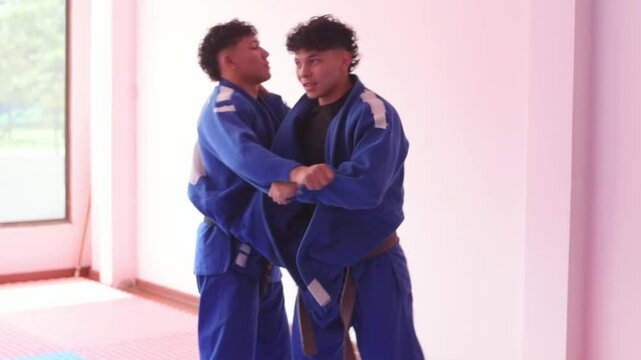 Judo partners warming up in dojo with blue dojo mat, window at background