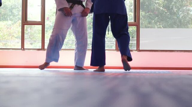 Unrecognizable judo fighters fighting in dojo with big windows at background