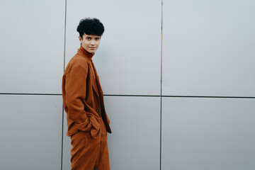 Stylish young man in brown outfit standing against a light gray wall, showcasing modern fashion...