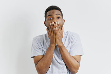 Shocked young african american man covering his mouth with hands in surprise on isolated white...