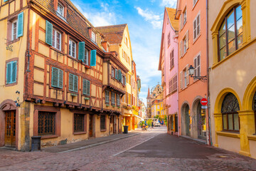 The picturesque colorful Grand Rue street of shops and cafes, with a tourist train in the distance, in the medieval old town of Colmar, France, in the Alsace wine region.	