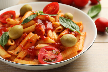Delicious pasta with tomato sauce, basil and olives in bowl on wooden table, closeup