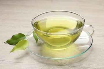 Refreshing green tea in cup and leaves on wooden table, closeup