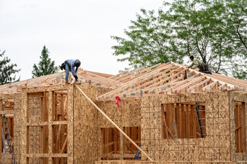 New residential home construction in framing stage, two workers on the roof rafters hard at work,...