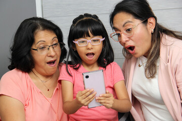 Latina brunette grandmother, mom and daughter use their cell phone to shop, watch movies, make...