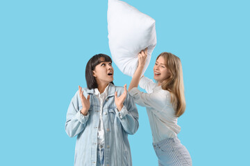 Young women fighting pillow on blue background