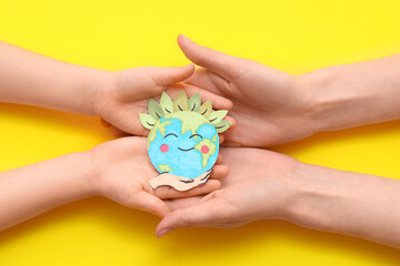 Child's and female hands with paper planet Earth on yellow background, closeup