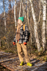 Fototapeta premium Happy relaxed woman basks in sunlight on face during eco trail walk in autumn forest. Female tourist hikes through natural landmarks, unity with nature on journey, domestic travelling, tourism