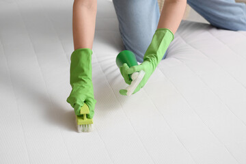 Young woman cleaning mattress with brush and detergent in bedroom, closeup