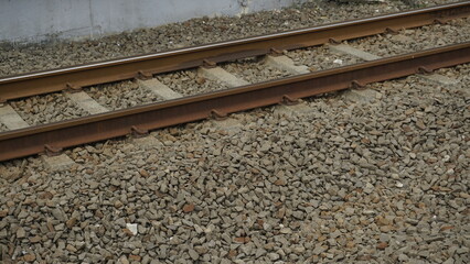 The gravel is around the train track at railway station on sunny day

