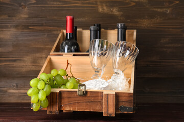 Box with bottles of wine, glasses, Camembert cheese and grapes on wooden background