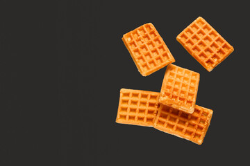Flying tasty Belgian waffles on black background