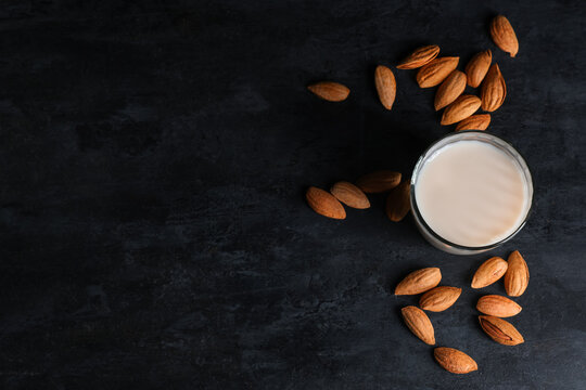 Glass of fresh almond milk and nuts on black background