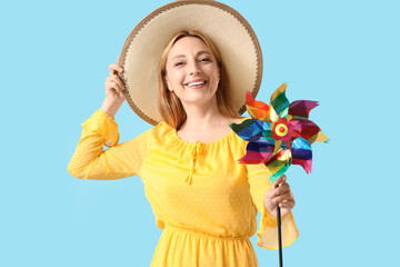 Mature woman in hat with toy windmill on blue background