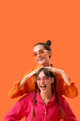 Beautiful young happy fashionable sisters in stylish outfits on orange background