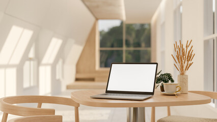 A laptop with a white-screen mockup on a wooden table in a contemporary minimalist room.