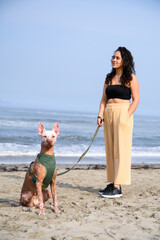 Young woman is enjoying a sunny day at the beach with her hairless xoloitzcuintli dog