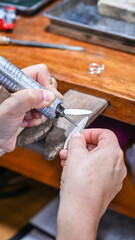 Goldsmith is working on a jewel on his workbench, engraving it with a rotary tool