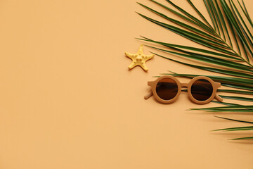 Stylish sunglasses with starfish and palm leaf on brown background