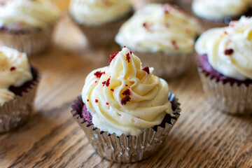 Red velvet cupcakes in silver foil on a wooden table.