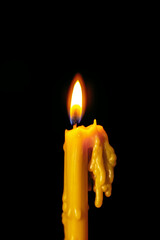 Yellow candle melting with flame on black background