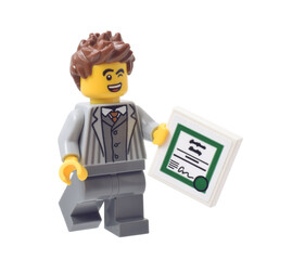 Fototapeta premium Lego minifigure of young businessman with certificate or reward closed up isolated on white. Editorial illustrative image of popular children plastic bricks