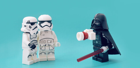 Fototapeta premium Lego minifigure of Darth Vader is taking a picture of two soldiers. Editorial illustrative image of popular children plastic bricks Star Wars. 