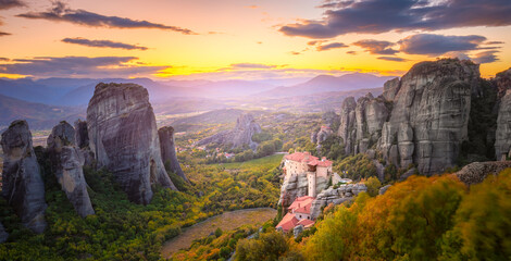 Panoramic landscape of Meteora, Greece at romantic sundown time with real sun and sunset sky. Meteora - incredible sandstone rock formations.  The Meteora area is on UNESCO World Heritage.