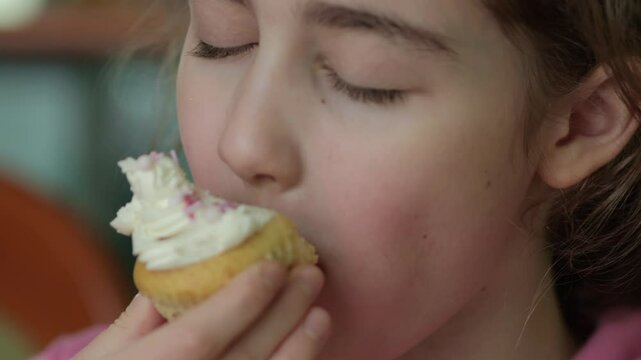 Child Eating Muffins Cupcakes Decorated With Sugar Cream. Girl Enjoying Vanilla Cupcakes with Frosting and Sprinkles. Unhealthy Junk Food. Hungry Sweet Tooth Child Bites Muffin with Sugar Frosting.