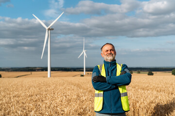 Man in a Vest Stands Confidently in a Golden Field With Wind Turbines Under Clouds