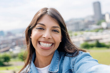 Smiling Woman Takes a Joyful Selfie in a City Park on a Sunny Day