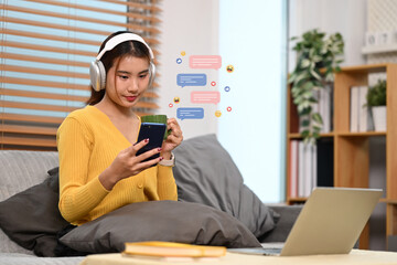 Beautiful young asian woman using mobile phone with chat bubbles and emojis floating over her device