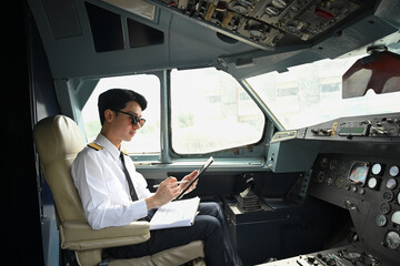 Handsome pilot wearing sunglasses using digital tablet, preparing for flight in the cockpit of an aircraft