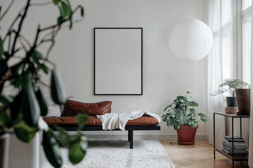 Frame mockup on a white wall in scandinavian natural style living room, brown leather ottoman, potted plants. Empty blank vertical din A poster with black frame in light room interior design