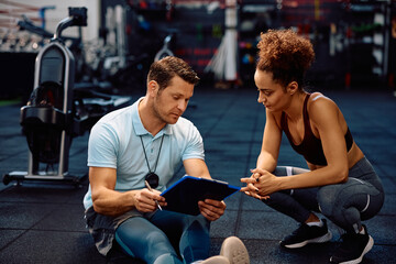 Personal instructor and sportswoman analyzing exercise plan in gym.