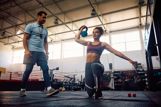 Athletic woman exercising with kettle bell during sports training with coach in health club.