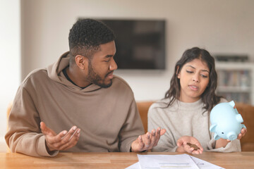 Young Couple Discussing Finances While Seated at Table With Piggy Bank in Hand