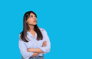 Obraz premium Woman in Striped Shirt With Crossed Arms Looking Thoughtfully Against Bright Blue Background